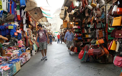 Fes Medina market with colorful bags and clothing stalls, Morocco.