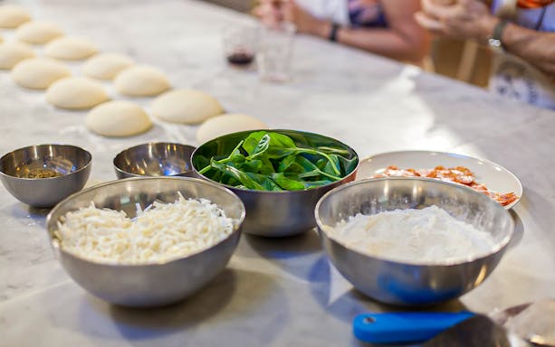 Pizza ingredients on a table for a cooking class, including dough, cheese, and basil.