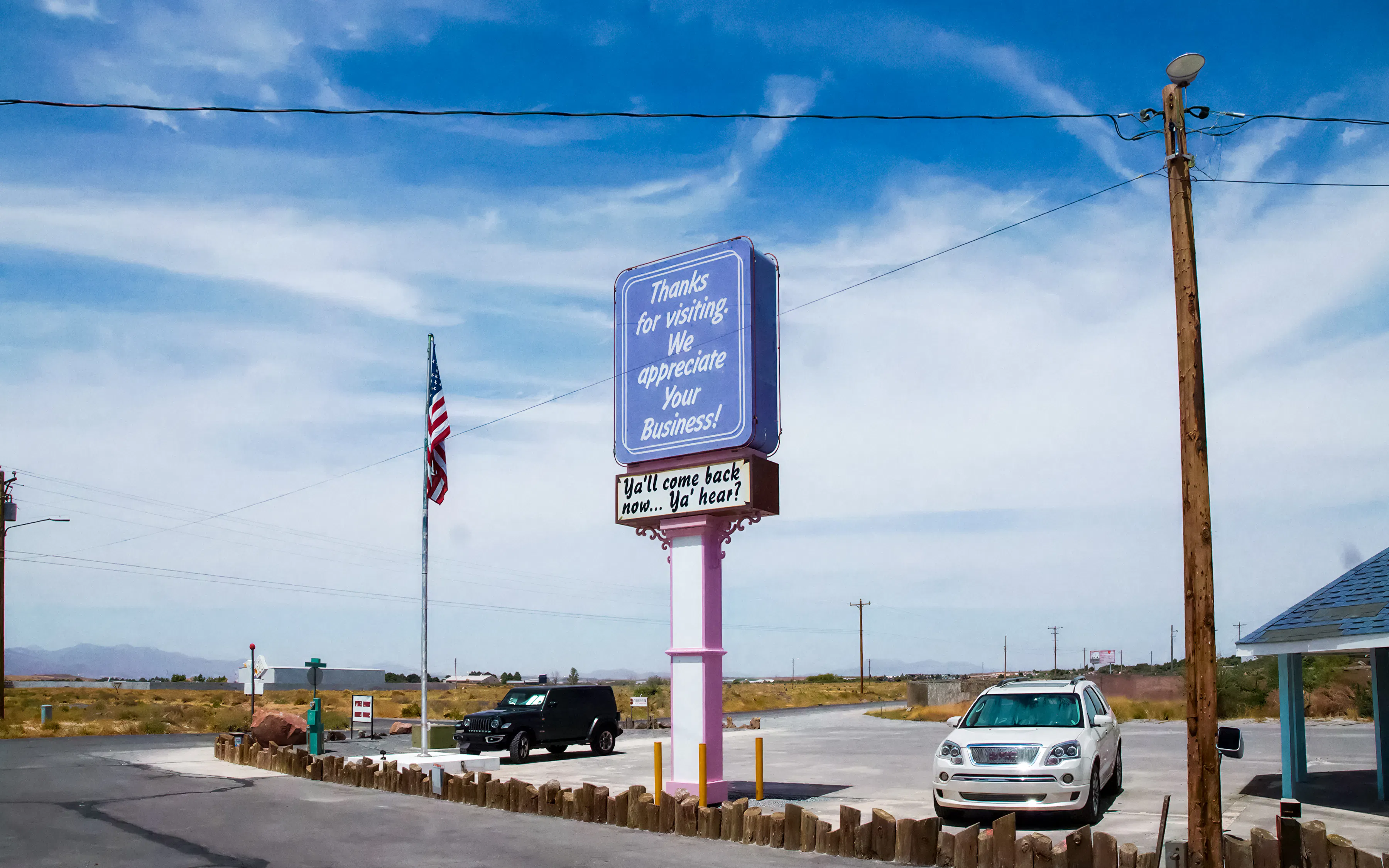 Sign at Chicken Ranch Brothel parking lot in Nevada with American flag nearby.