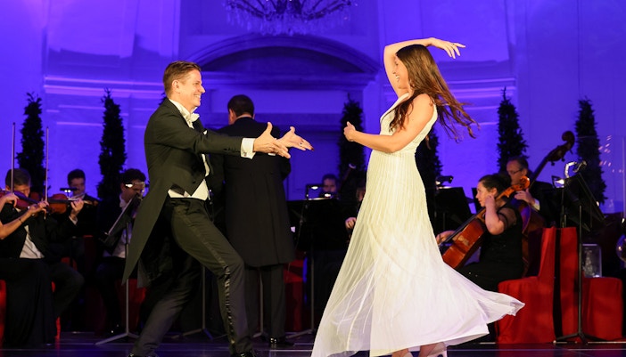 Dancers performing at Schonbrunn Palace concert with orchestra in the background.
