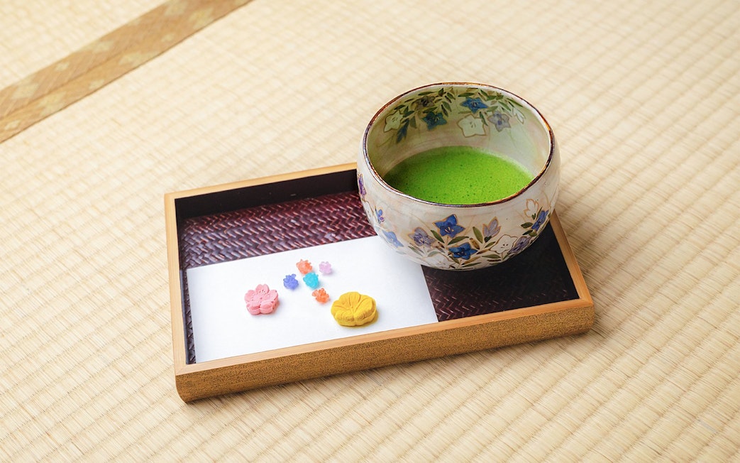 Ceramic bowl of matcha tea with traditional sweets on tatami mat in Machiya townhouse.