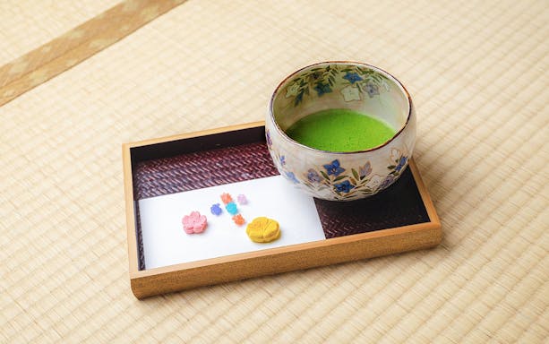 Ceramic bowl of matcha tea with traditional sweets on tatami mat in Machiya townhouse.