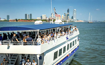 Tourists on a sightseeing cruise in New York Harbor with city skyline in the background.