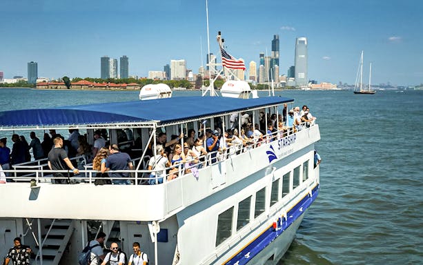 Tourists on a sightseeing cruise in New York Harbor with city skyline in the background.
