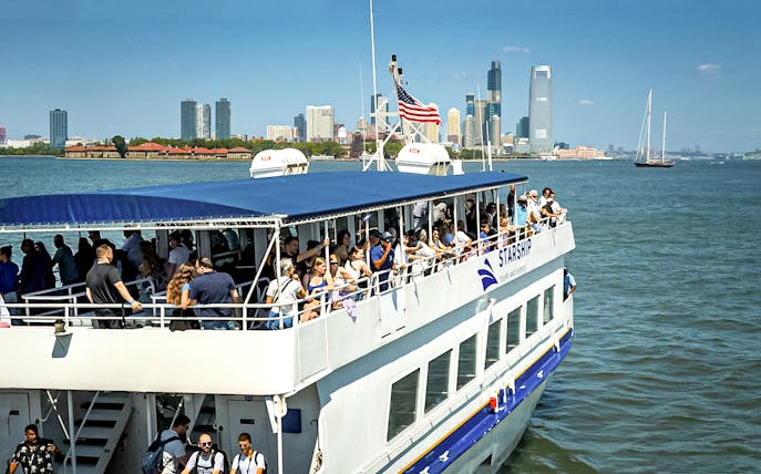 Tourists on a sightseeing cruise in New York Harbor with city skyline in the background.