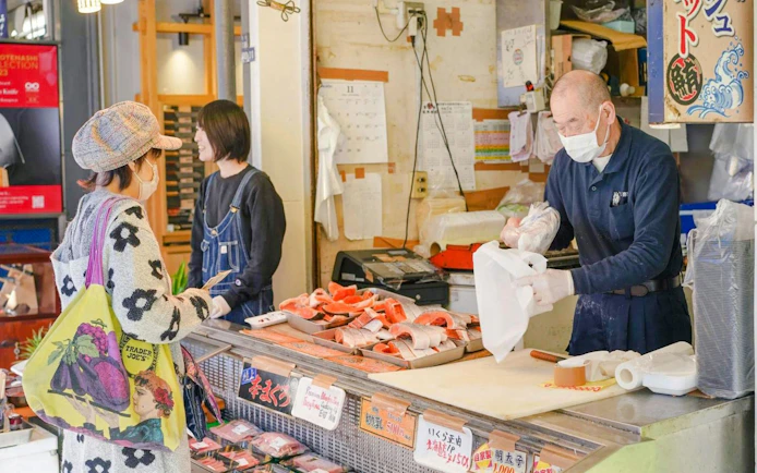 Storefront vendor at Tsukiji Fish Market preparing seafood for a customer.