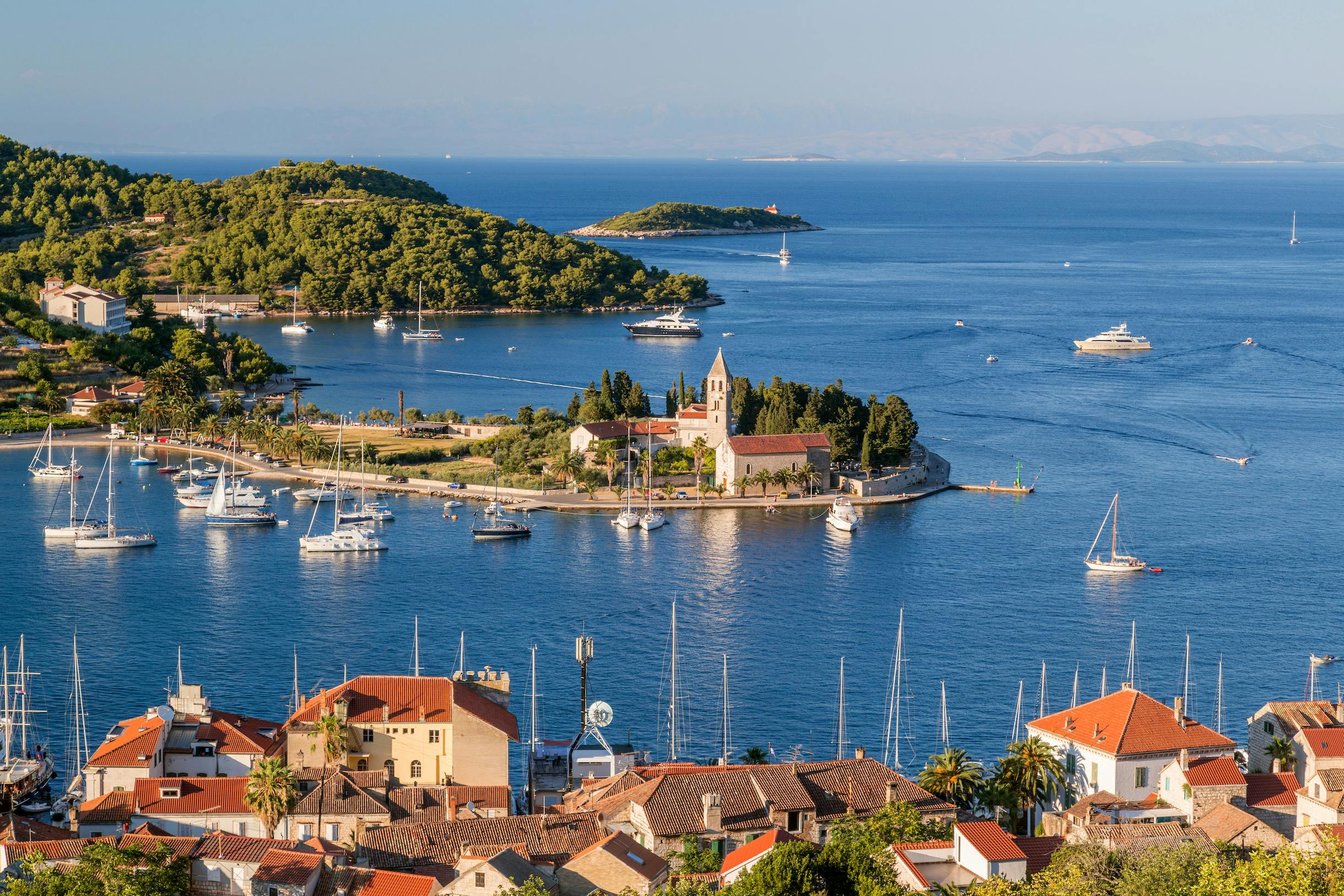Boats in the harbor near a historic church on Vis Island, Croatia.