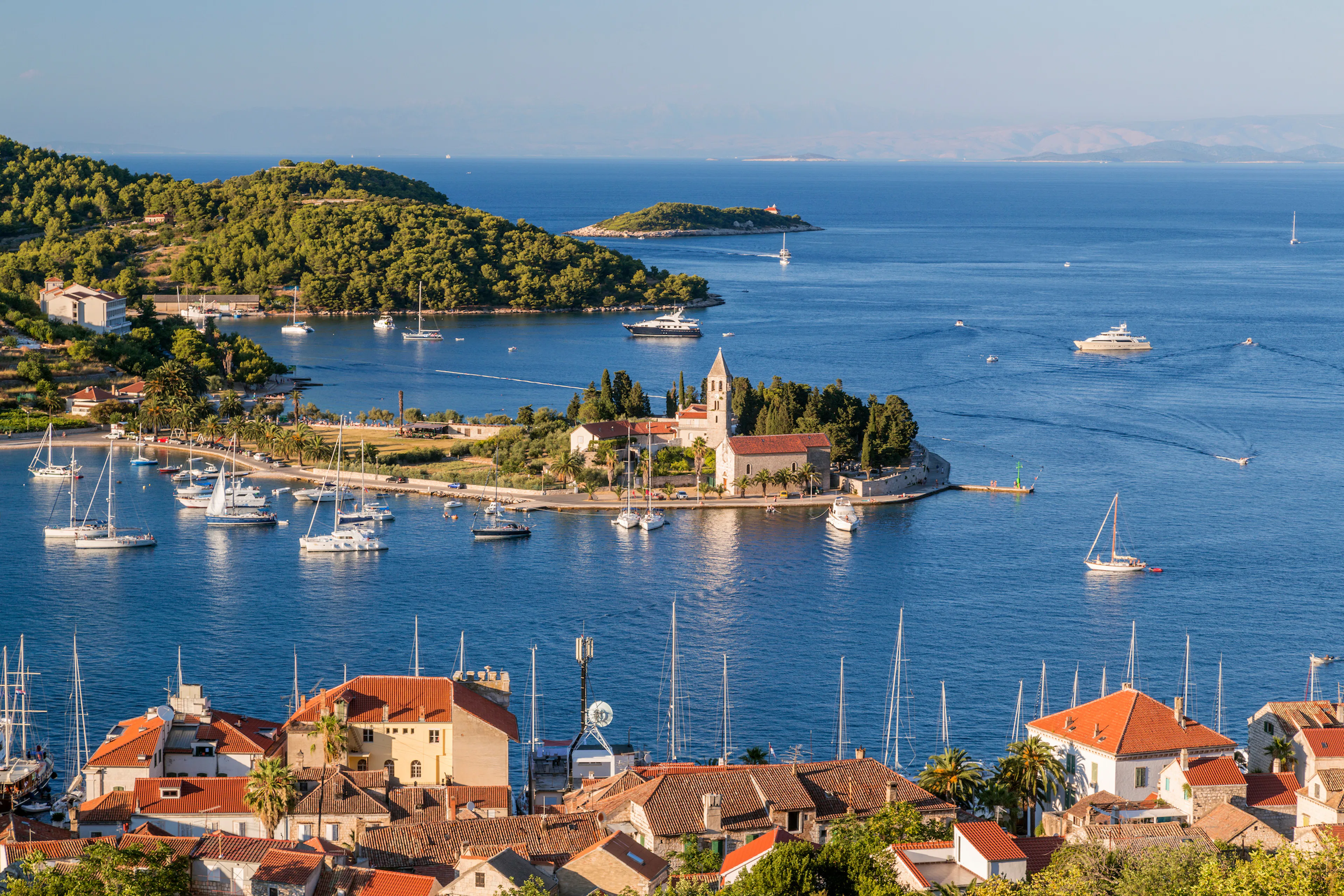 Boats in the harbor near a historic church on Vis Island, Croatia.