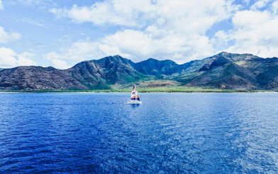 Sailboat on West Oahu waters with mountainous backdrop during whale watch tour.