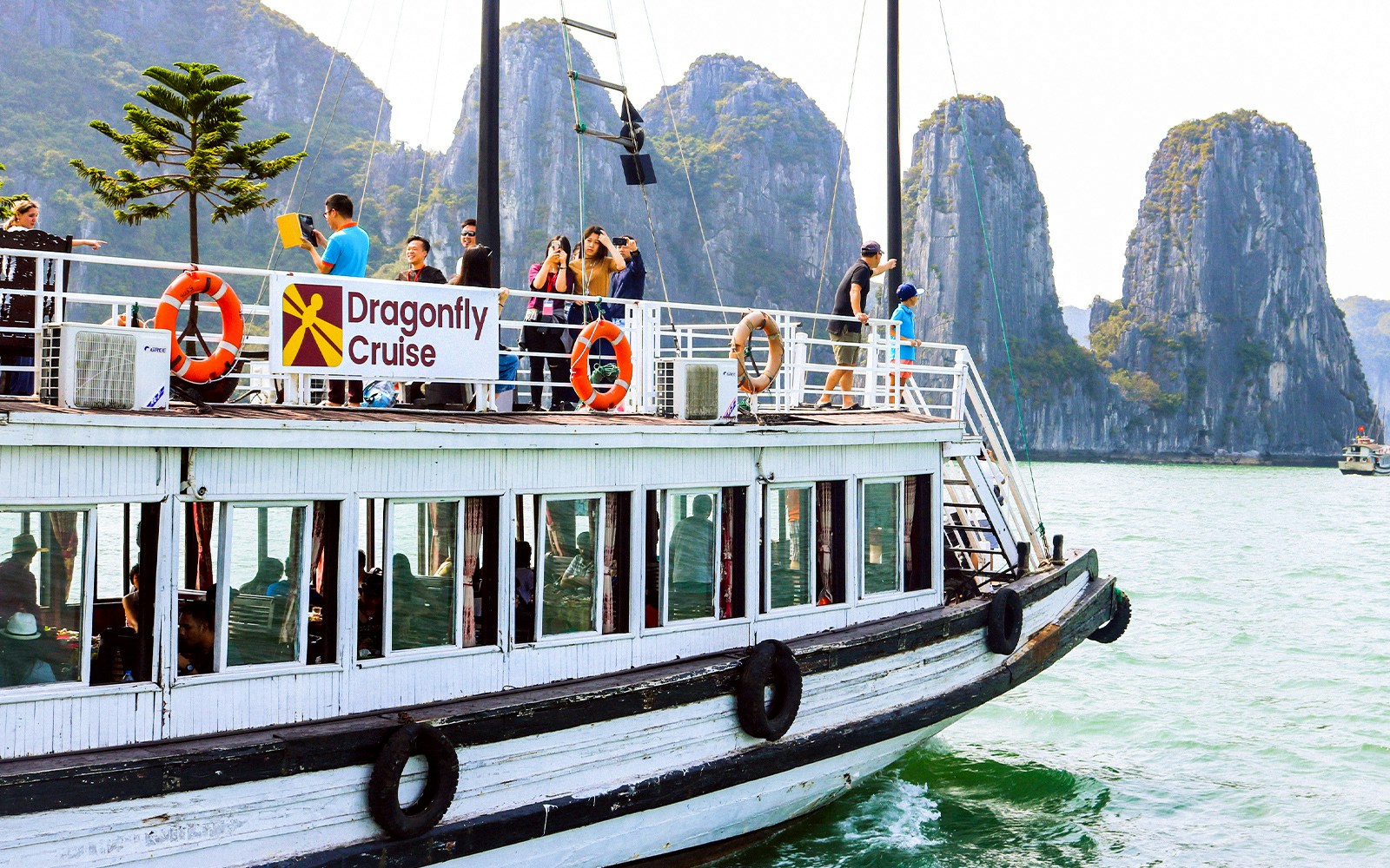 Dragonfly Cruise boat with tourists in Halong Bay, limestone karsts in background.
