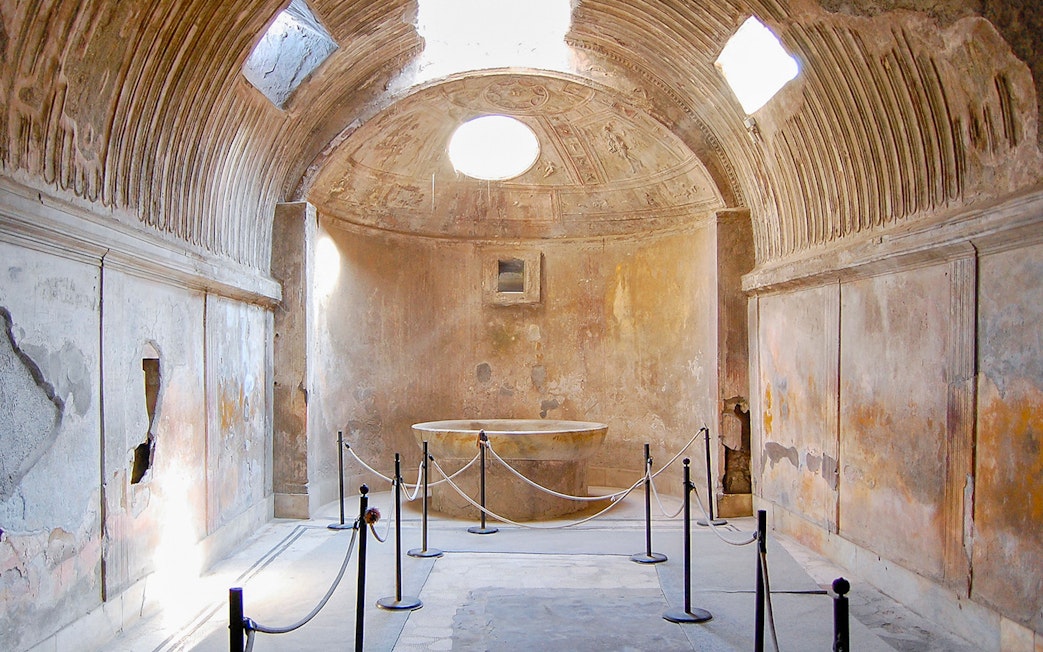 Ancient bathhouse interior in Pompeii with stone basin and vaulted ceiling.