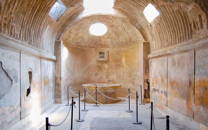 Ancient bathhouse interior in Pompeii with stone basin and vaulted ceiling.