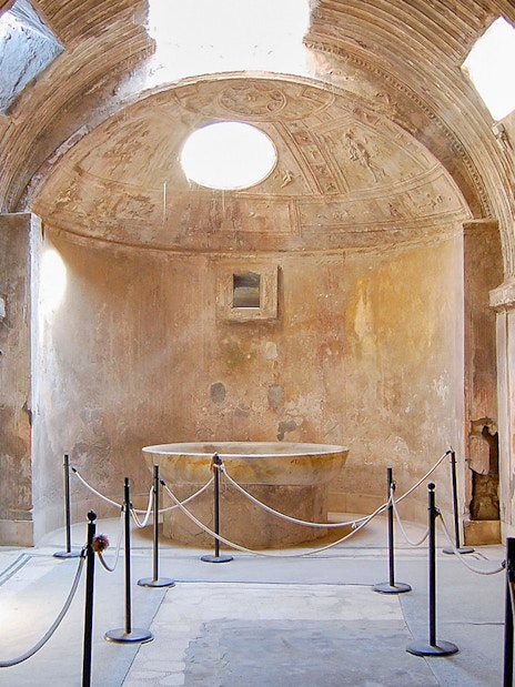 Ancient bathhouse interior in Pompeii with stone basin and vaulted ceiling.