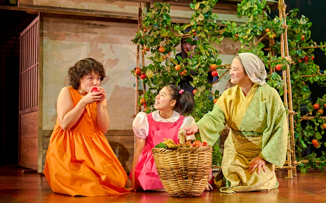 Three actors in colorful costumes on stage with a basket of fruit, My Neighbour Totoro production.
