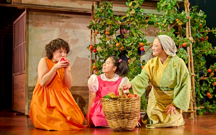 Three actors in colorful costumes on stage with a basket of fruit, My Neighbour Totoro production.