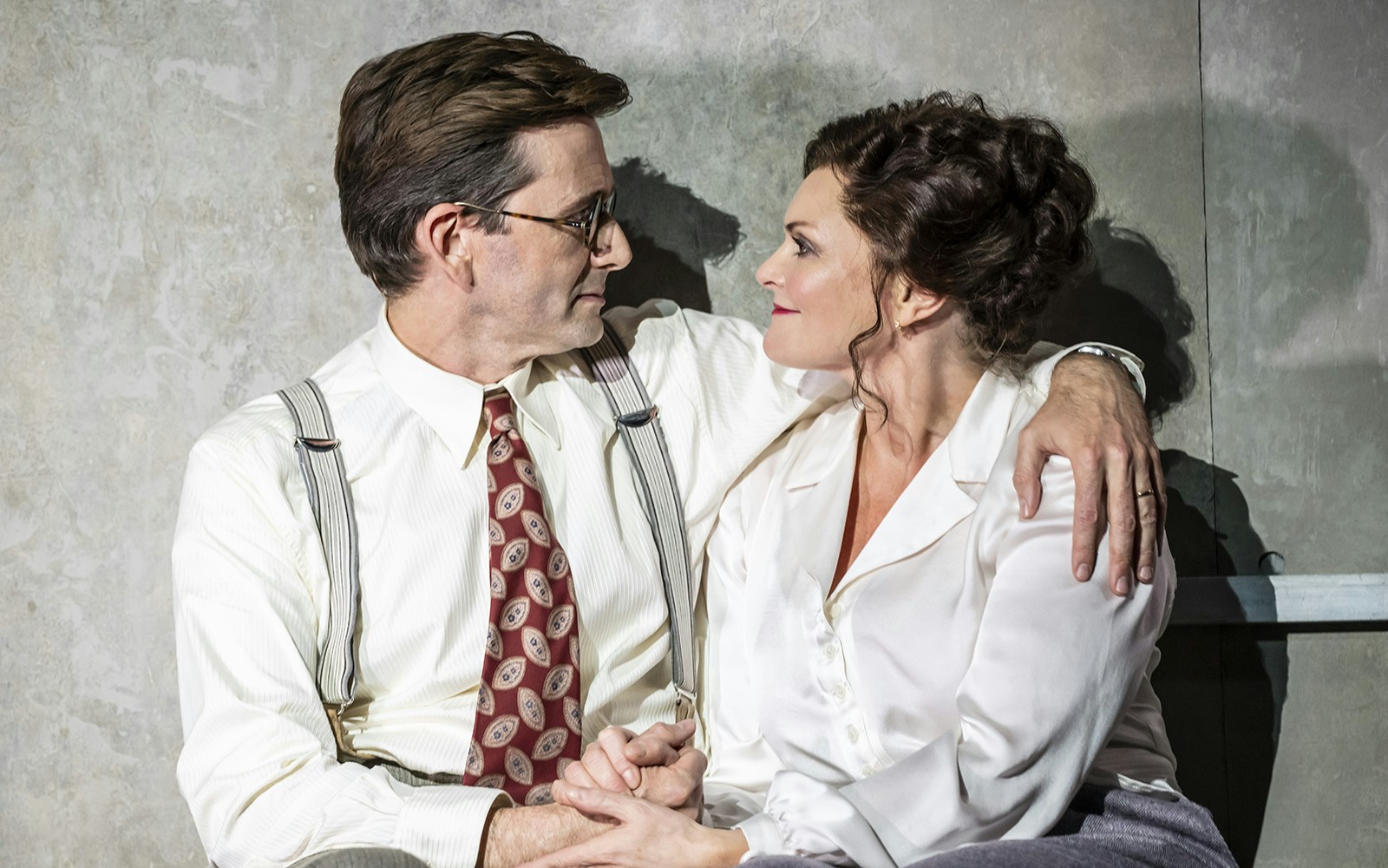 A man and woman in vintage attire share an intimate moment on stage.