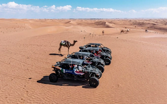 Desert landscape with four-seater buggies and camels, showcasing a safari experience.
