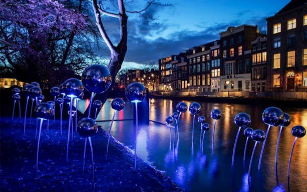 Amsterdam Light Festival installation with glowing spheres along a canal at dusk.