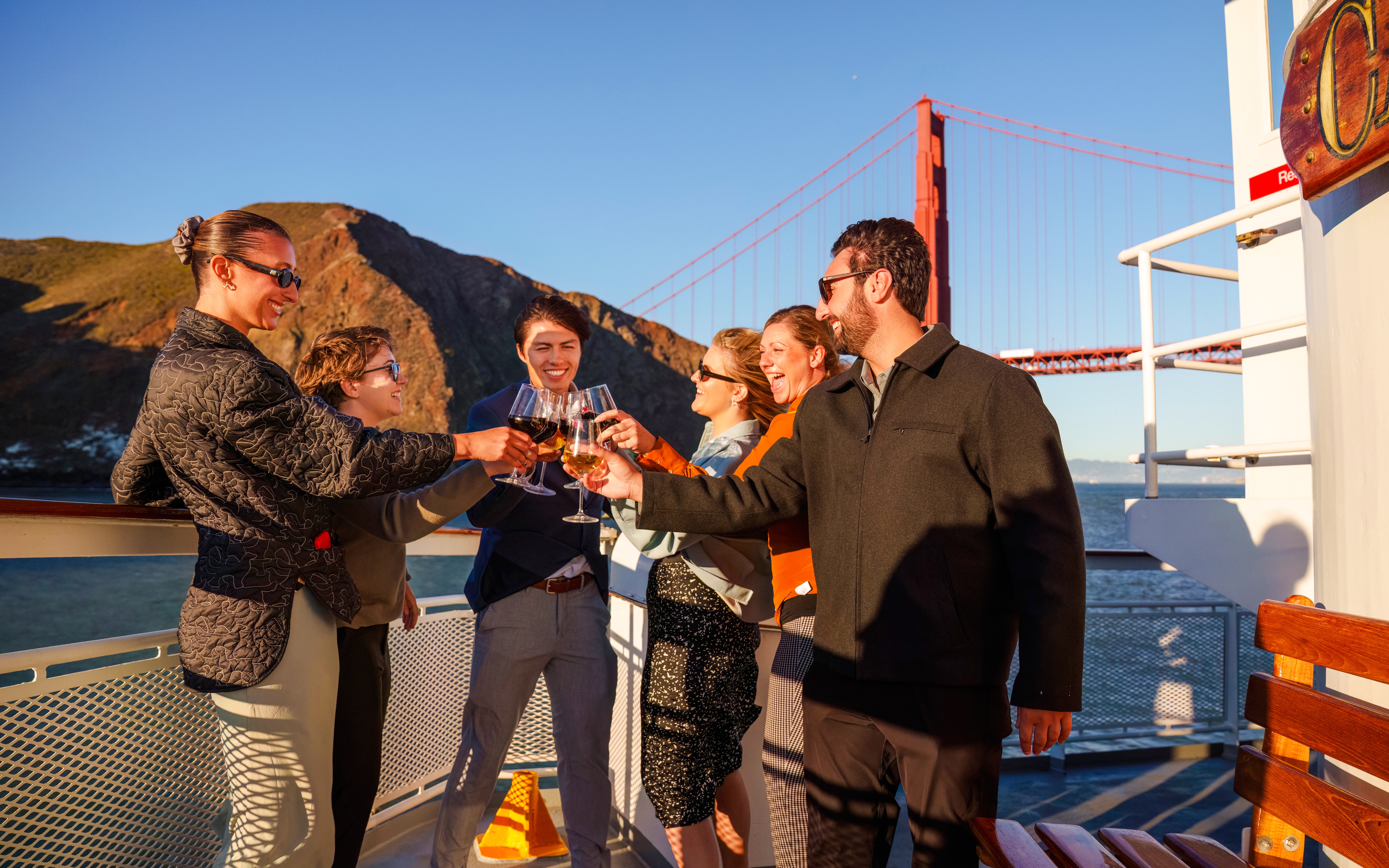 Group toasting on a San Francisco dinner cruise with Golden Gate Bridge in background.