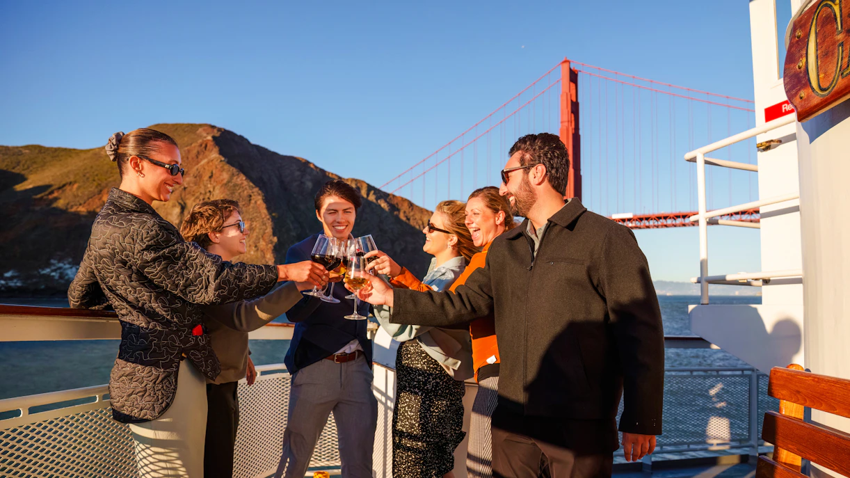 Group toasting on a San Francisco dinner cruise with Golden Gate Bridge in background.