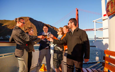 Group toasting on a San Francisco dinner cruise with Golden Gate Bridge in background.
