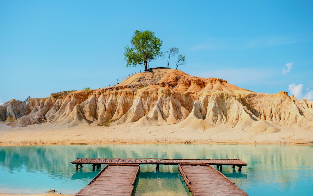 Wooden pier leading to Blue Lake with sandy cliffs in Bintan, Indonesia.