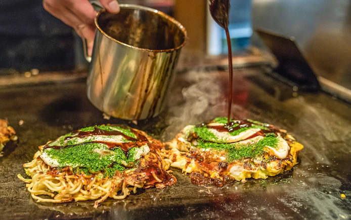 Okonomiyaki being prepared on a grill during a Hiroshima and Miyajima bus tour.