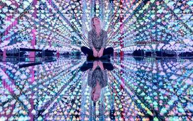 Person sitting in a colorful mirrored room at Moco Museum.