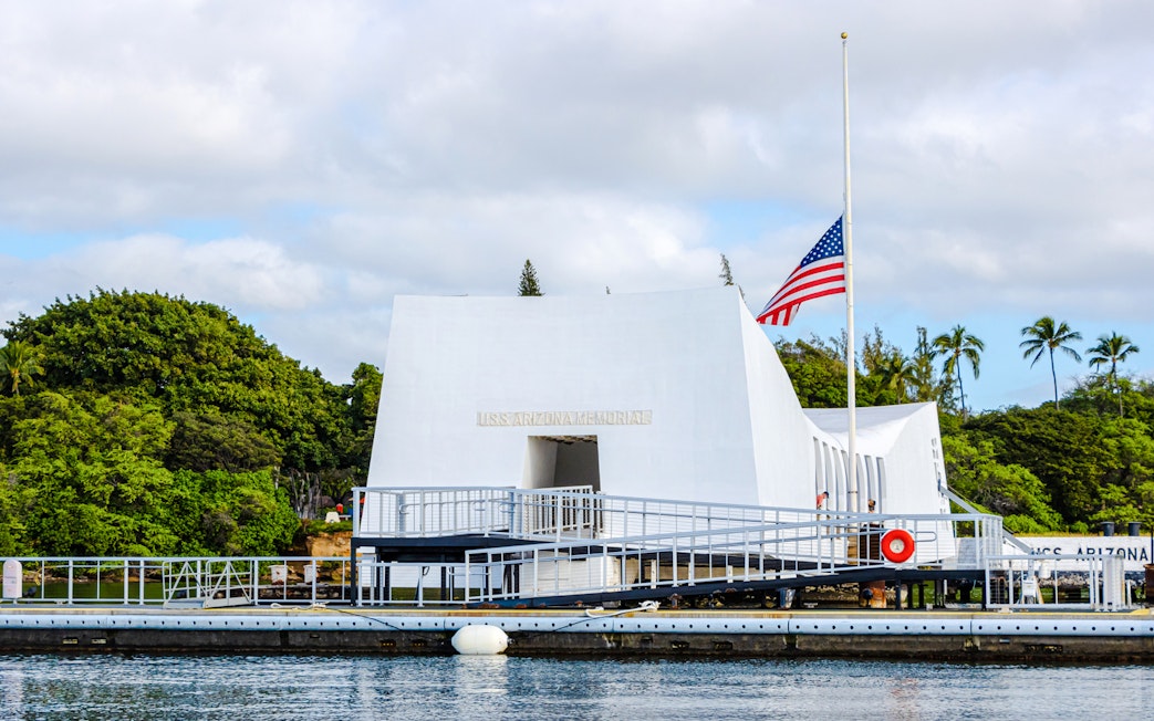 USS Arizona Memorial in Pearl Harbor with American flag and surrounding greenery.