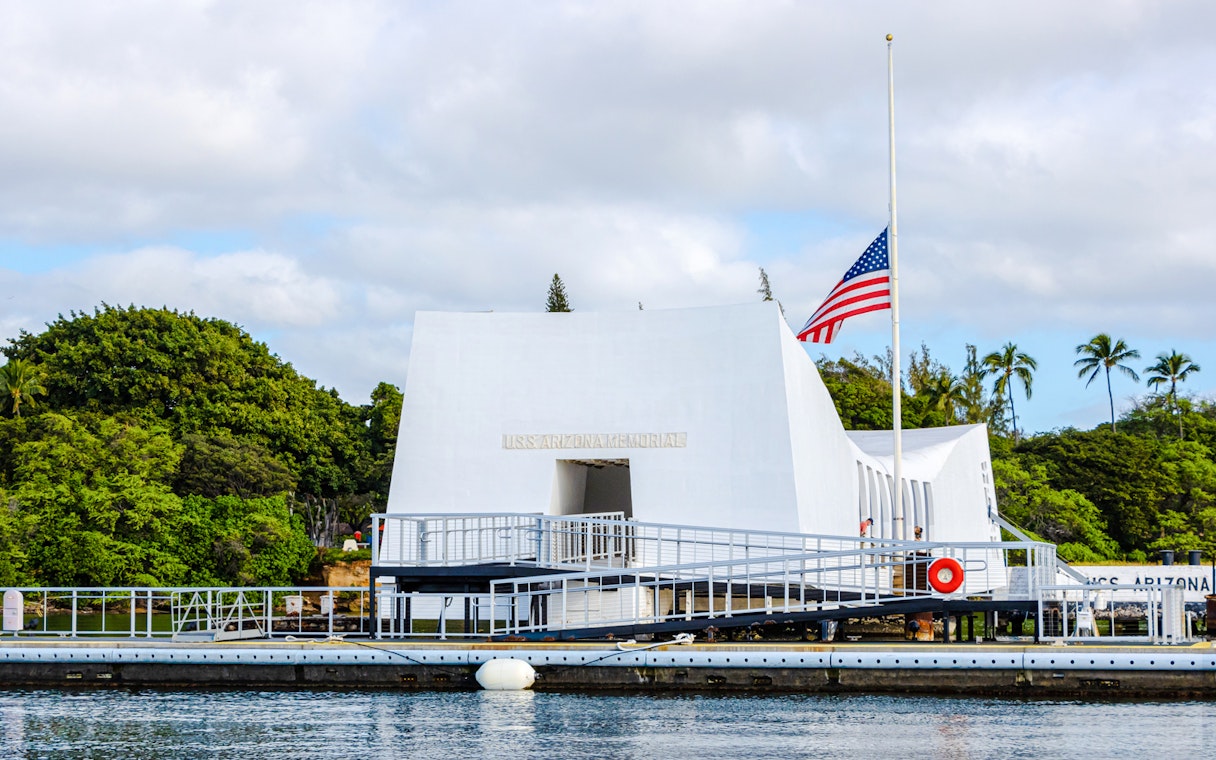 USS Arizona Memorial in Pearl Harbor with American flag and surrounding greenery.