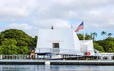 USS Arizona Memorial in Pearl Harbor with American flag and surrounding greenery.