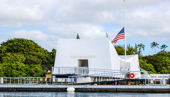 USS Arizona Memorial in Pearl Harbor with American flag and surrounding greenery.