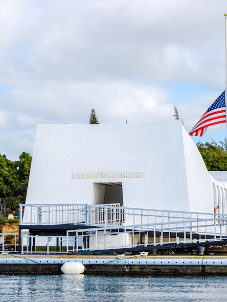 USS Arizona Memorial in Pearl Harbor with American flag and surrounding greenery.