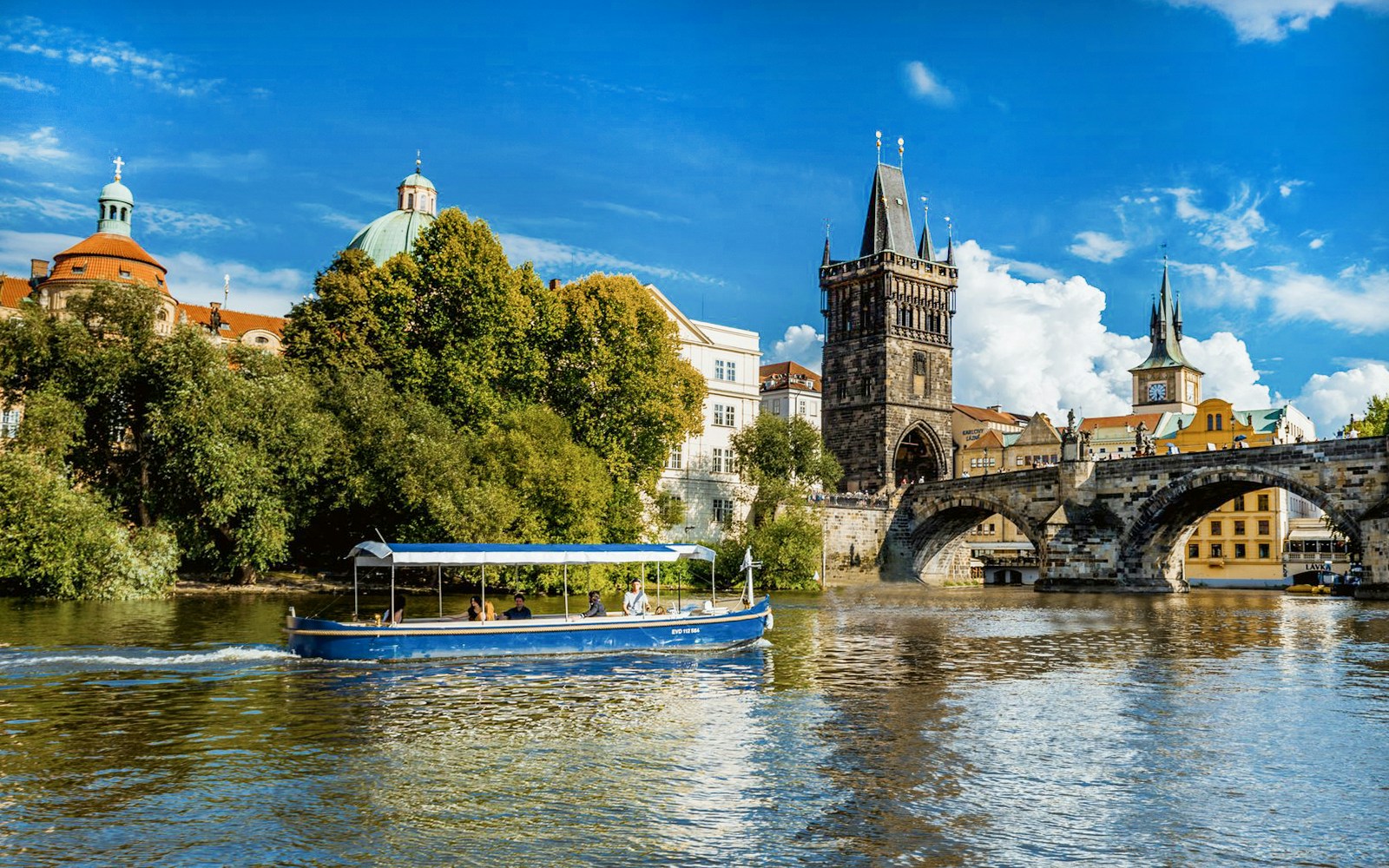 Sightseeing cruise boat navigating Devils Channel in Prague with historic buildings lining the waterway.