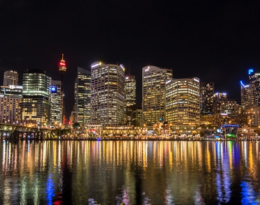 Sydney skyline at night with illuminated skyscrapers reflecting on Cockle Bay.