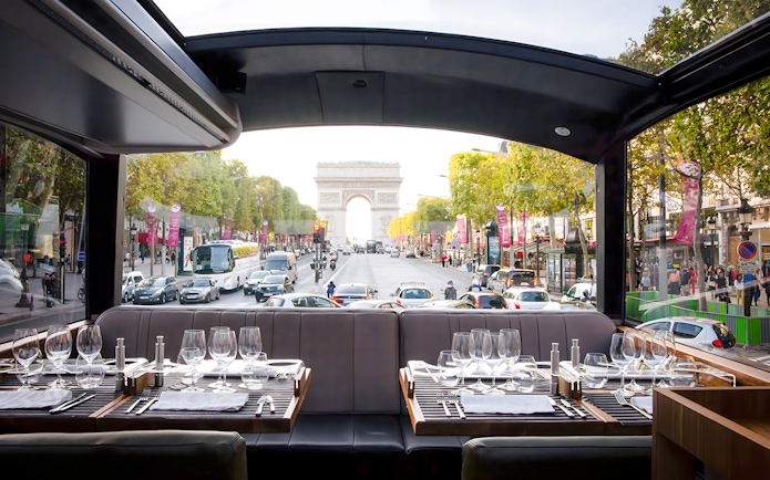 Dining setup inside Bustronome Paris with view of Arc de Triomphe.
