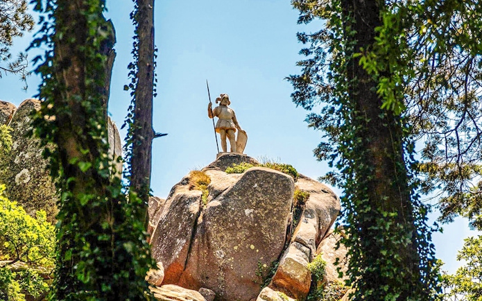 Statue of the Warrior on a rocky hill in Pena Palace Park, surrounded by trees.