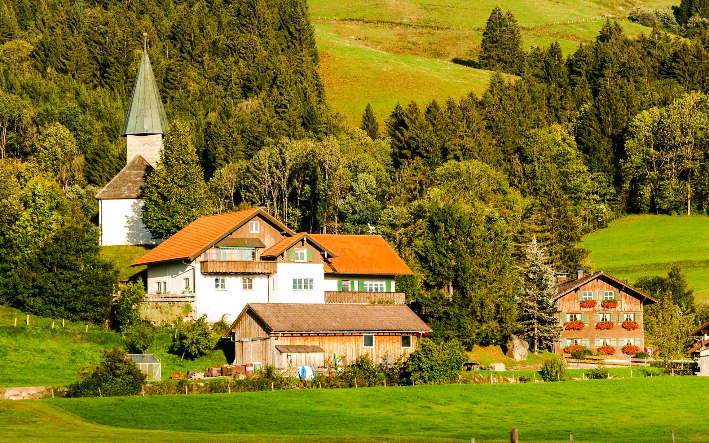 Bavarian village with traditional houses and church surrounded by lush greenery.