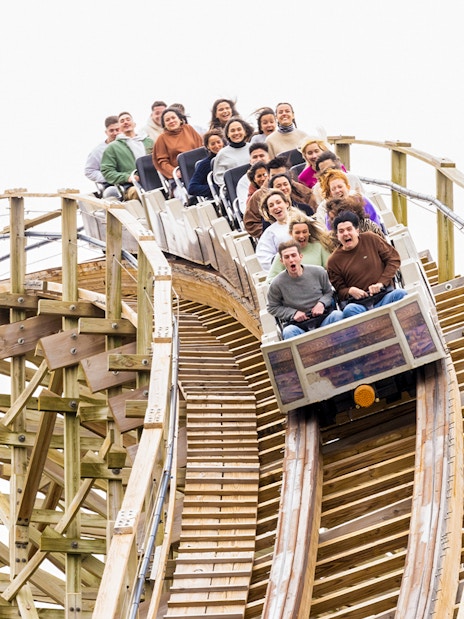 Riders on Coaster Express at Parque Warner Madrid descending a wooden track.