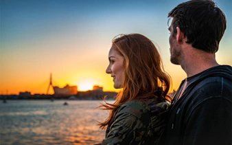 Couple enjoying sunset on a Boston sightseeing cruise with city skyline in background.