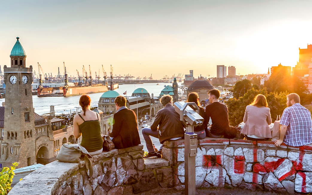 People enjoying sunset view of Hamburg harbor with clock tower and Elbe River.