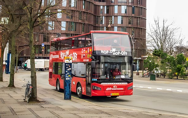 Copenhagen hop-on hop-off tour bus on city street near modern building.
