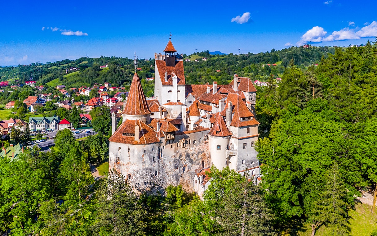 Bran Castle in Romania with iconic towers and medieval architecture surrounded by lush greenery.