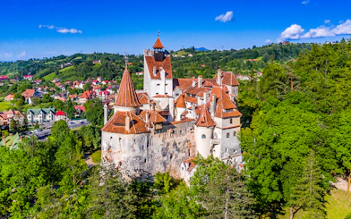 Bran Castle in Romania with iconic towers and medieval architecture surrounded by lush greenery.