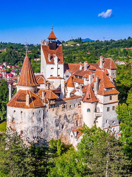 Bran Castle in Romania with iconic towers and medieval architecture surrounded by lush greenery.
