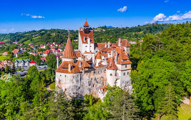 Bran Castle in Romania with iconic towers and medieval architecture surrounded by lush greenery.
