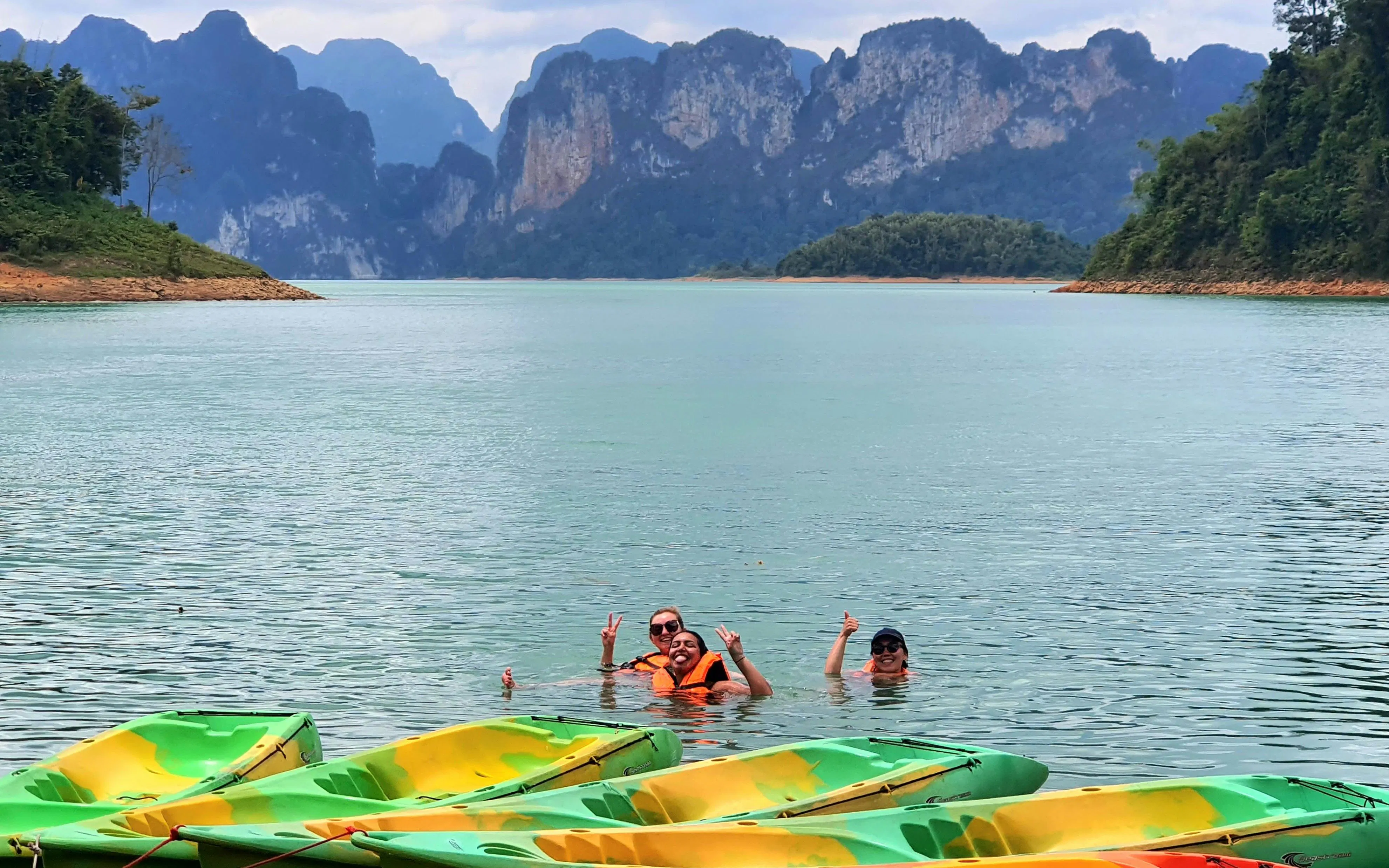 Kayakers swimming in Cheow Lan Lake with limestone cliffs in the background, Krabi tour.