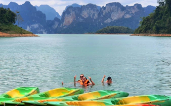 Kayakers swimming in Cheow Lan Lake with limestone cliffs in the background, Krabi tour.