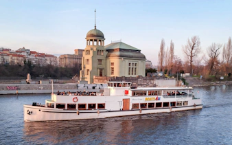 Historic cruise boat on Vltava River passing by a riverside building in Prague.