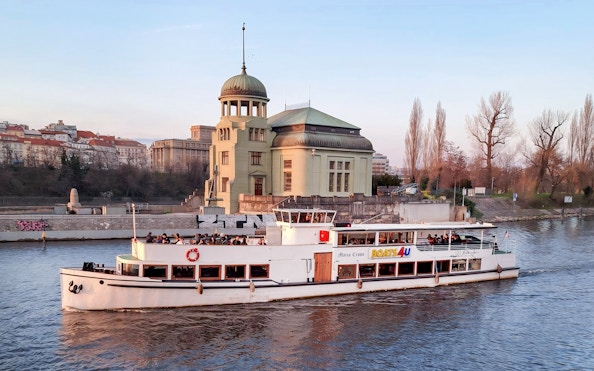 Historic cruise boat on Vltava River passing by a riverside building in Prague.